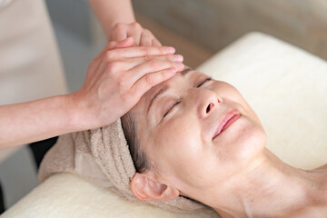 Woman relaxing during a facial massage with hands on her forehead and eyes closed, towel wrapped around her head