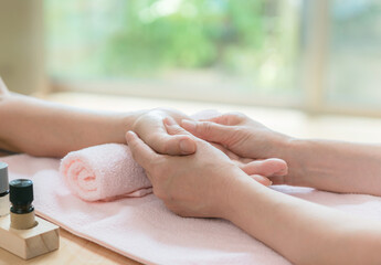 Close-up of a hand massage being performed on a pink towel in a bright spa setting, with a small bottle nearby.