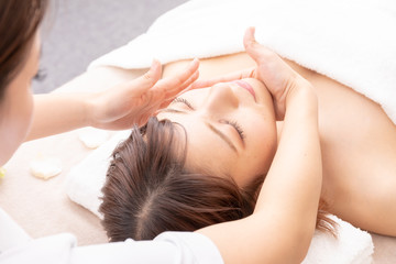 Woman relaxing during a facial treatment; therapist massages her forehead as she lies on a spa bed.