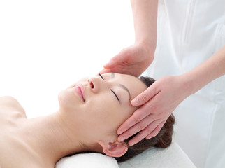 Woman lying on a massage table with eyes closed as a therapist massages her temples and scalp area.