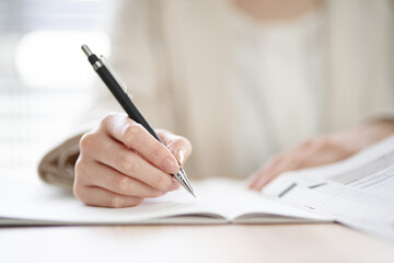 Close-up of a hand holding a pen and writing in a notebook on a desk.