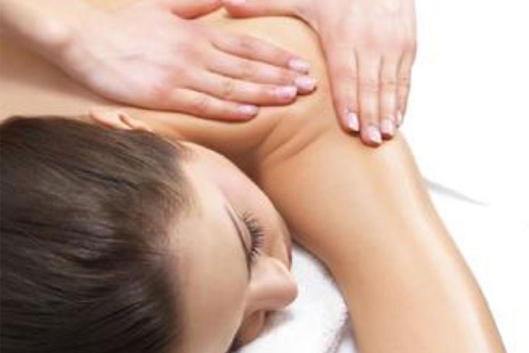 Person lying face down receiving a shoulder and upper back massage from a therapist; hands kneading the area