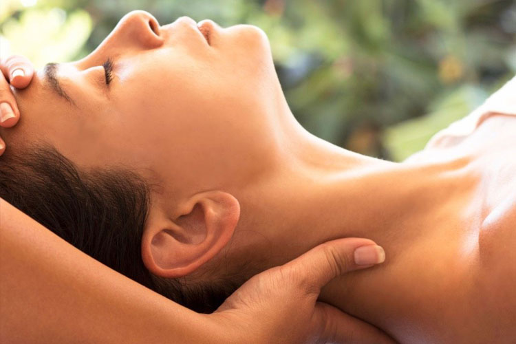 Close-up of a person receiving a neck massage outdoors, hands cradling their neck.