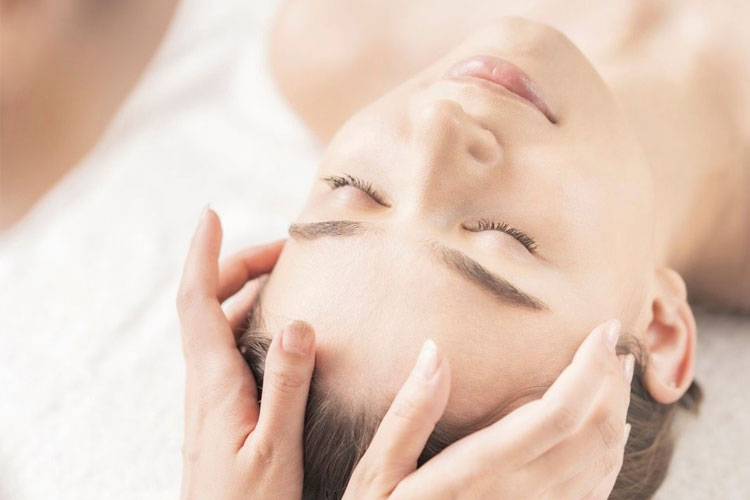 Relaxing spa moment: hands cradle the client's temples during a facial massage with eyes closed