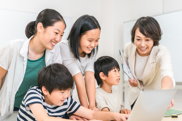 Group of adults and children gathered around a laptop, smiling as they review something on the screen.