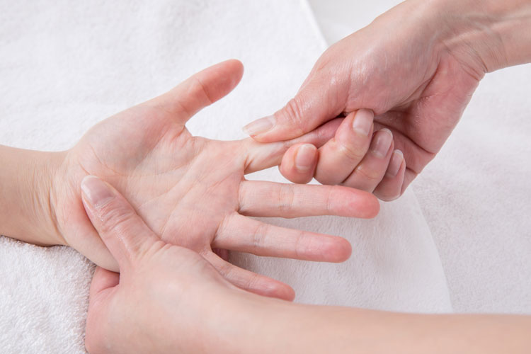 Close-up of a hand being gently massaged on a white towel surface, showing a palm up and another hand applying pressure.
