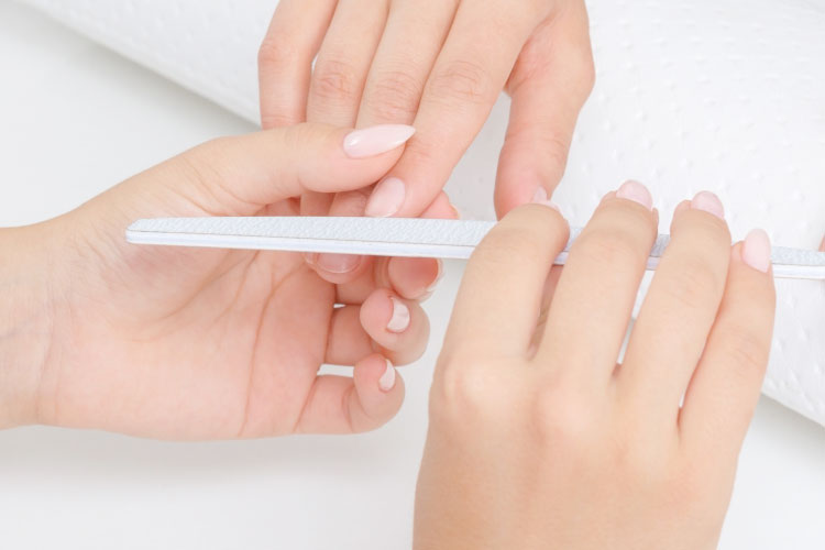Close-up of hands filing fingernails with a white emery board during a manicure
